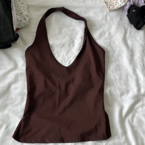 Brun halterneck linne - Säljer ett brunt halterneck linne med djup v-ringning och smickrande passform. Toppen är ärmlös och har en enkel, stilren design som passar perfekt till jeans eller kjol. Materialet känns mjukt och stretchigt, vilket gör den bekväm att bära hela dagen.