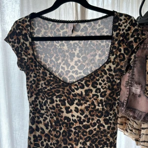 Leopardmönstrad topp från Nelly - Säljer en topp/t-shirt med leopardmönster och v-ringning. Denhar korta ärmar och är figurnära i modellen. Perfekt för dig som vill sticka ut med ett djurmönster.