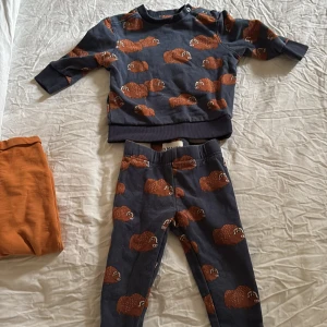 Blå barnleggings med myskoxar D.M.D - Supersöta blå leggings från D.M.D by denim day i storlek 80, med gulligt tryck av bruna myskoxar över hela byxan. Mjukt bomullsmaterial och resår i midjan för skön passform. Perfekta för lek och bus!