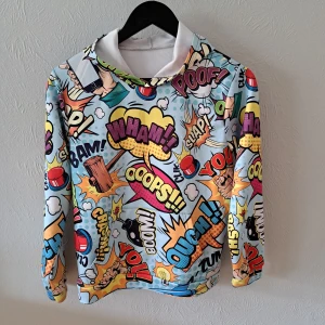 Färgglad hoodie med comic print - Säljer en supercool hoodie med färgglatt comic book-mönster och massor av serietidningsuttryck som WHAM, OUCH och BAM. Tröjan har huva, lång ärm och är gjord i mjuk polyester. Storlek 160. Bundlerabatt finns 🌟