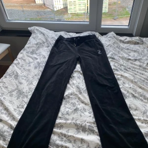 Svarta mjukisbyxor från Juicy Couture - Säljer ett par klassiska svarta mjukisbyxor från Juicy Couture med dragsko i midjan och broderad logga fram. Baktill står det 'Juicy' i stora bokstäver. Byxorna är raka i modellen och tillverkade i mjuk polyesterblandning. 