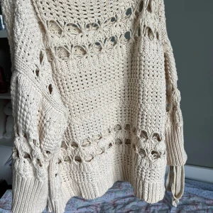 Beige stickad tröja från Zara - Säljer en beige stickad tröja från Zara med grovstickat mönster och dekorativa hål samt knytband i midjan. Tröjan har långa ärmar och bred ribbad mudd vid ärmslut och halsringning. Perfekt för lager-på-lager-stil.