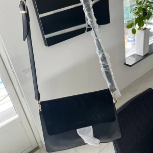 Damväska - Säljer en helt ny svart Damväska som är perfekt för vardagen. Väskan är svart med ett band och är perfekt för dig som gillar enkelt men snyggt. Väskan säljs för ett bra pris då den inte är till användning längre. Först till kvarn