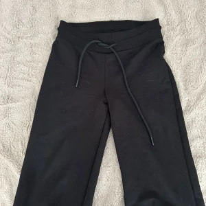 Svarta mjukisbyxor - Svarta mjukisbyxor med dragsko i midjan. Byxorna har en enkel och clean design, raka ben och är tillverkade i mjukt material som känns skönt mot huden. Perfekta för chill dagar eller när du vill vara bekväm.