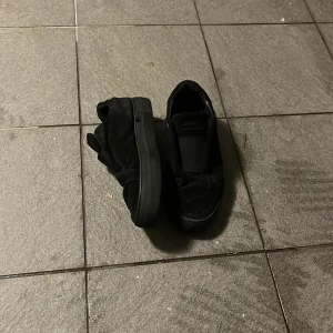 Svarta slip-on sneakers från Arigato - Svarta slip-on sneakers från Arigato med elastisk panel över vristen och diskret logga på sidan. Skorna har en platt sula och är tillverkade i textil med detaljer i syntet. Perfekta för en clean och stilren look.