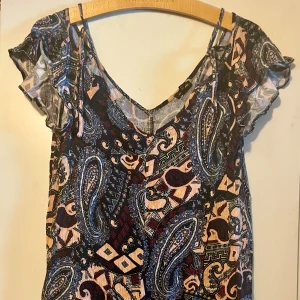 Paisleymönstrad kort klänning från River Island i stl 40 - Somrig kortare mönstrad tunn klänning i stl 14/40. Vringad, korta volangärmar. Normal i storlek.  Färger: svart, lila, blå, ljusrosa.  Använd fåtal ggr, inget att anmärka på.  