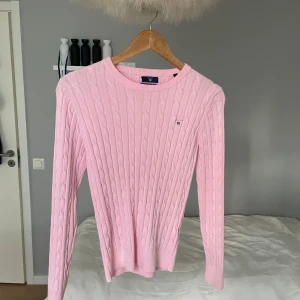kabelstickat tröja från Gant.  - Säljer en klassisk kabelstickad tröja från GANT i en fin pastellrosa färg. Mjuk, skön och perfekt för både vardag och mer preppiga outfits. GANT-logga broderad på bröstet.  📏 Storlek: S 🧶 Material: Bomull 🧼 Skick: Mycket fint skick, knappt använd – inga noppor eller fläckar. 💸 Nypris ca 1 200–1 500 kr