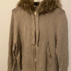 Beige stickad cardigan jacka med fuskpäls - Beige stickad cardigan med luva och fuskpäls runt kanten som man kan ta av och sätta på. Den är i storlek 36/38🫶🏽💞 