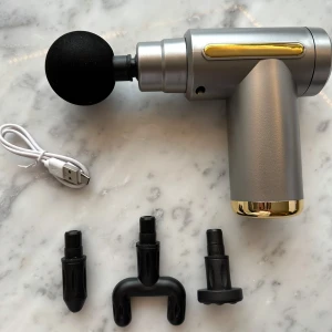 Massagepistol med olika munstycken - En silverfärgad massagepistol med gulddetaljer och fyra utbytbara munstycken samt en USB-laddningskabel. Perfekt för att massera olika muskelgrupper. Kompakt och lätt att använda.