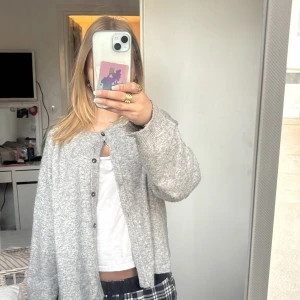 Grå stickad kofta med knappar - Mysig grå stickad kofta med rund hals och knäppning framtill. Koftan har en loose passform och långa ärmar, perfekt att slänga på sig över en t-shirt. Enkel och stilren design som funkar till det mesta.