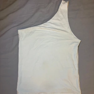 Vit oneshoulder topp Gina Tricot - Säljer en stilren vit oneshoulder topp från Gina Tricot i mjuk bomull. Toppen har en asymmetrisk axelbandslös design med en axel och är perfekt för dig som gillar minimalistisk och trendig stil.