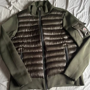Grön Moncler cardigan herr L - Snygg grön cardigan från Moncler i storlek L. Jackan har en fin front i blankt material, stickade ärmar och detaljerad Moncler-logga på ärmen. Dragkedja framtill och fickor med dragkedja. Perfekt för dig som vill ha en stilren och exklusiv look. Är 192 och väger 80 så skulle säga att den passar som M, priset går att diskuteras vid snabb affär.