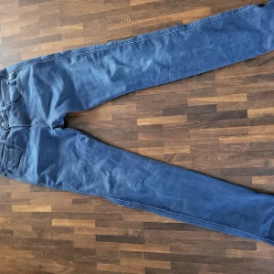 Blå Replay Anbass jeans herr - Säljer ett par blå Replay Anbass jeans med smal passform. Klassisk femficksmodell, normal midja och raka ben. Jeansen är tillverkade i stretchig denim för extra komfort och har snygga detaljer vid fickorna.