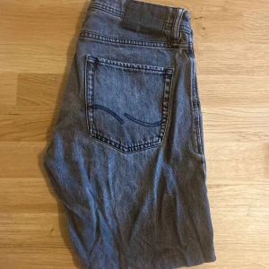 Grå jeans från Jack & Jones - Säljer ett par klassiska grå jeans från Jack & Jones. Byxorna har fem fickor, raka ben och normal passform. Perfekta för dig som gillar en enkel och stilren look. Jeansmaterialet är mjukt och bekvämt.
