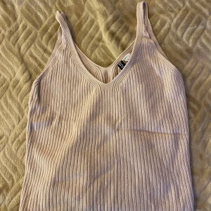 Beige ribbad linnetopp - Säljer en beige ribbad linnetopp från H&M med v-ringning och smala axelband. Perfekt för varma dagar eller som layering-plagg. Supermjuk och stretchig i materialet.