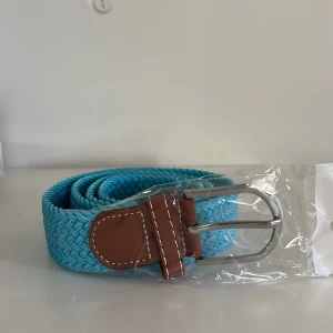 Turkost flätat bälte  - Säljer ett turkost flätat bälte med bruna skinn-detaljer och silverspänne. Perfekt accessoar för att ge din outfit lite extra färg. Bältet har en klassisk design med kontrastsömmar på skinnet.