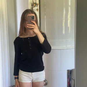 Svart stickad topp med knappar - Svart fin topp med knappar en bit ner, trekvartsärmar och bred halsring. Går typ att ha off one shoulder om man vill det. Skönt material och inte jättevarm. 