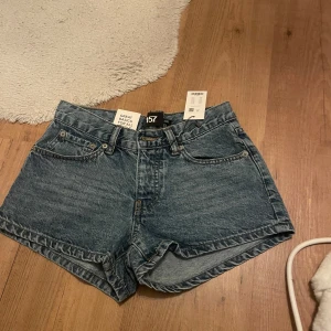 Blå jeansshorts med broderad detalj från 157 - Säljer ett par blå jeansshorts från lager 157. Baksidan har snygga broderade mönster på fickorna som ger en liten touch! Perfekta för sommaren och lätta att matcha med allt. helt nya med prislappen på!