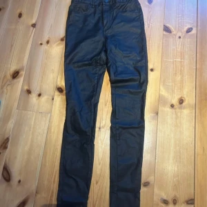 Svarta skinny jeans - Säljer ett par svarta skinny skinnbyxor med klassisk femficksdesign och hällor för bälte. Jeansen har en smal passform och är tillverkade i ett stretchigt material som sitter tajt längs benen. Perfekta för en stilren och enkel look.