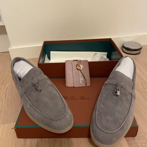 Grå/beige loro piana summer Walk loafers - Snygga grå loafers i mocka från Loro Piana med klassisk design och dekorativ detalj på ovansidan. Skorna har rund tå och platt sula, perfekta för en stilren look.