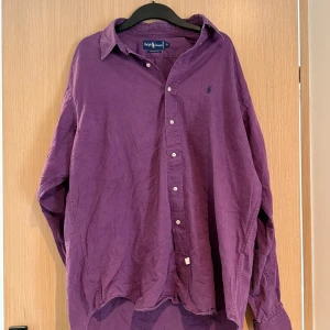 Lila skjorta från Ralph Lauren XL - Säljer en lila skjorta från Ralph Lauren i storlek XL. Skjortan är i 100% bomull, har klassisk krage, knäppning framtill och långa ärmar. Den har en avslappnad passform och den ikoniska lilla loggan broderad på bröstet.