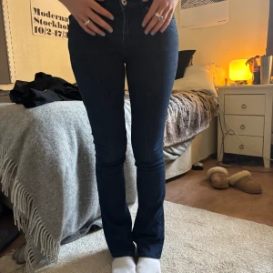 Mörkblå bootcut jeans - Säljer ett par mörkblå jeans med bootcut-modell och klassisk femficksdesign. Jeansen har låg midja och stängs med dragkedja och knapp. Perfekta för dig som gillar en tidlös och stilren look.