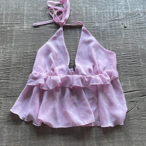 Ljusrosa volang topp med knyt - Söt ljusrosa topp med volangkant och knyt i nacken. Toppen är ärmlös och har en luftig, säljer då den inte kommer till användning💗