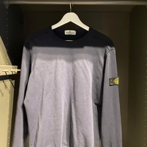 Blå långärmad tröja från Stone Island Junior - Säljer en stilren blå långärmad tröja från Stone Island Junior. Tröjan har klassisk rund halsringning och den ikoniska Stone Island-loggan på vänster ärm. Perfekt för dig som gillar streetwear och vill ha något bekvämt och snyggt.