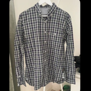 Rutig skjorta från Polo Jeans Company - Snygg rutig skjorta från Polo Jeans Company i blått, grönt och vitt. Klassisk button-down krage, långa ärmar och knäppning framtill. Skjortan är i bomull och har märkets logga på sidan. Perfekt för dig som gillar en avslappnad men stilren look.