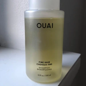 OUAI Fine Hair Shampoo 300 ml - OUAI Fine Hair Shampoo i en frostad plastflaska på 300 ml. Schampot är ljusgult och passar för tunt hår. Innehåller stärkande keratin, biotin och chiafröolja för att ge volym och styrka. Snygg minimalistisk design med svart text på flaskan.