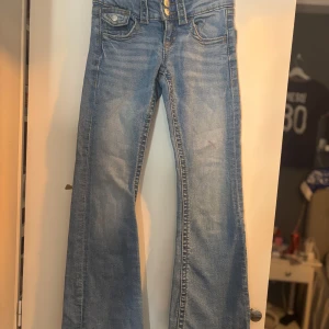 Blåa lågmidjade jeans - Ljusblå bootcut jeans från Gina Tricot med klassisk femficksdesign och dubbla knappar i midjan. Dom har en liten fläck (se sista bilden) men det är inte jätte synlig när man väll har på sig byxorna och går säker att tvätta bort om man verkligen försöker!