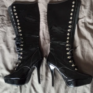 Svarta platåstövletter från Fantasy stl 6 - Höga svarta stövletter i glansigt syntetmaterial från Fantasy Shoes London. Skorna har spetsig tå, platåsula och hög klack. Snörning framtill med metallöglor ger en edgy look. Perfekta för dig som vill sticka ut med en statement-stövel. Storlek 6 vilket typ passade min stl 38. Använt dem 2-3ggr.