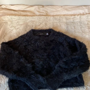 Svart fluffig stickad tröja Vero Moda - Mysig svart stickad tröja från Vero Moda i storlek XS. Tröjan har en fluffig och lite lurvig yta som ger en cool och trendig look. Perfekt för dig som gillar oversized känsla och vill ha något varmt och stilrent till hösten eller vintern.