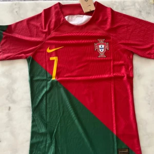 Portugal Ronaldo 7 fotbollströja Nike - Portugal landslagströja från Nike med Ronaldo och nummer 7 på ryggen. Tröjan är röd och grön med gula detaljer, kortärmad och tillverkad i Dri-Fit material för bästa komfort. Slim fit-modell med broderat landslagsmärke och Nike-logga.