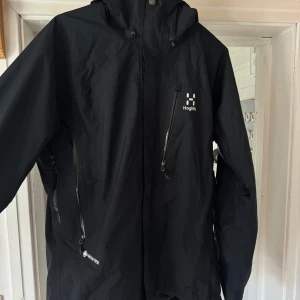 Svart skaljacka från Haglöfs - Säljer en svart skaljacka från Haglöfs i storlek M. Jackan har huva, dragkedjor framtill och på fickorna samt GORE-TEX-material som står emot regn och vind. Perfekt för utomhusaktiviteter och äventyr. Helt fläck fri. 