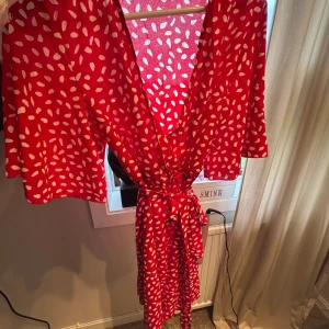 Röd omlottklänning med vita prickar - Superfin röd omlottklänning med vita prickar och knyt i midjan. Klänningen har v-ringning, korta vida ärmar och ett flowy fall. Perfekt för dig som vill sticka ut med färg och mönster! Hör av er om bild på hur den ser ut på