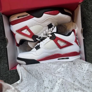 Nike Air Jordan 4 red cement 45 - Säljer ett par Nike Air Jordan 4 red cement  med vit ovandel i skinn, röda och svarta detaljer samt meshpaneler på sidorna. Skorna har klassisk snörning, synlig Air-sula och Jumpman-logga på plösen och hälen. Perfekta för dig som vill sticka ut med en ikonisk sneaker.  Dom är storlek 46 men passar mig som har 45
