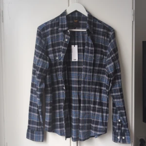 Blårutig skjorta från Lee, regular fit - Snygg blårutig skjorta från Lee i regular fit. Skjortan har klassisk krage, långa ärmar och knäppning framtill. Tillverkad i mjuk bomull och passar perfekt till jeans eller chinos. Fickor med lock på bröstet och coolt rutmönster i blått och svart.
