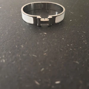 Vitt armband med H-detalj från H - Snyggt armband i silverfärgad metall med vita paneler och ikonisk H-formad låsdetalj från H. Perfekt accessoar för att lyfta din stil med en lyxig touch.
