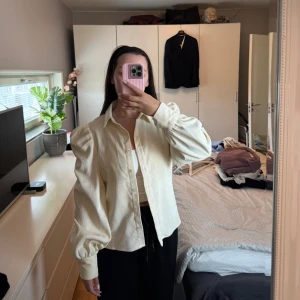 Äggvit/ljusgul skjorta med puffärmar - Säljer en ljusgul/äggvit skjorta med klassisk krage och puffiga långärmar. Skjortan har knappar framtill och är tillverkad i Manchestermaterial. Väldigt fin och klassisk skjorta som är lite tjockare i materialet. Använd vid ett tillfälle.