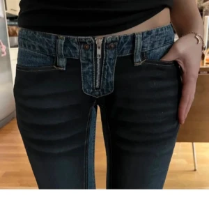 Unika blå jeans med låg midja och dragkedja - Säljer ett par blå jeans med låg midja och markerad dragkedja framtill. Byxorna har en annorlunda design med bred linning och dubbla knappar. Modellen är bootcut och materialet är klassisk denim.