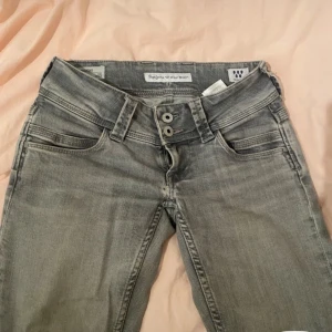 Grå pepe jeans  - Säljer ett par grå jeansbyxor med låg midja och dubbla knappar framtill. Byxorna har klassisk femficksdesign och tillgjorda bootcut ben som hon ja köpte av sytt sjölv be om mer bidler då detta e dessa jag har just idag eftersom jeansen är hos min kompis ❤️. Perfekta för en avslappnad och stilren look. Low waist  jeansen har några defekter som ja lägger in bilder på irmgom 
