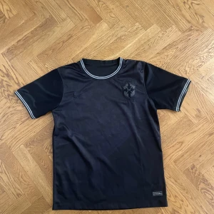 Svart Brasil Nike fotbollströja - Snygg svart Brasil fotbollströja från Nike med diskret mönster och broderat CBF-emblem på bröstet. Tröjan har rund hals med grå och svarta ränder samt korta ärmar med matchande detaljer. Tillverkad i lätt och ventilerande polyester, perfekt för träning eller match.