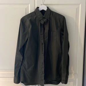 Mörkgrön skjorta från Massimo Dutti - Snygg mörkgrön skjorta från Massimo Dutti i stretchig bomull. Klassisk modell med knappar hela vägen, lång ärm och bröstficka. Perfekt för dig som gillar stilrena och enkla plagg med bra passform. Storlek S som är on spot storleksmässigt. Passar även M. Använd ca. 3 gånger och är i väldigt bra skick. Nypris 1100kr. Priset kan diskuteras.