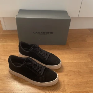 Svarta sneakers från Vagabond - Stilrena svarta sneakers från Vagabond med ovandel i mocka och klassisk snörning. Skorna har en vit platt sula som ger en snygg kontrast mot det svarta. Perfekta för dig som gillar en enkel men trendig look.