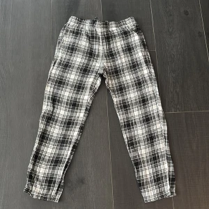Svarta och vita rutiga byxor H&M S - Snygga rutiga byxor från H&M i svart och vitt. De har elastisk midja och är gjorda i mjuk bomull, perfekta för en chill och avslappnad stil. Passformen är loose och mönstret är klassiskt rutig, vilket ger en cool vibe till outfiten.
