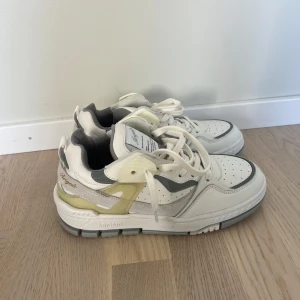 Axel Arigato sneakers i vitt och grått - Chunky sneakers från Axel Arigato i vitt, grått och ljusgult. Skorna har detaljer i skinn och mocka, perforerad tå och tjock sula. Helt nya och oanvända 
