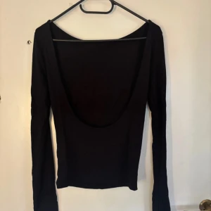 Svart långärmad topp Gina Tricot - Svart långärmad topp från Gina Tricot med djup, öppen rygg. Snygg och enkel design som sitter tight och har en klassisk rund halsringning framtill. Perfekt att styla med jeans eller kjol för en trendig look.