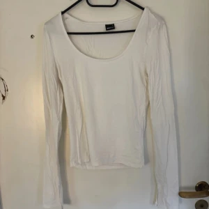 Vit långärmad topp Gina Tricot - En basic vit långärmad topp från Gina Tricot med rundad, djup urringning. Tunn och mjuk i bomullsmix, perfekt att styla med jeans eller kjol. Enkel och stilren design som funkar till många looks.