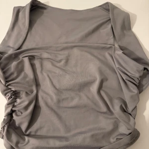 Grå offshoulder topp  - Snygg grå offshoulder topp med draperade sidor. Tunn och stretchig, perfekt för en trendig look. Passformen är tight och toppen har en stilren, minimalistisk design.